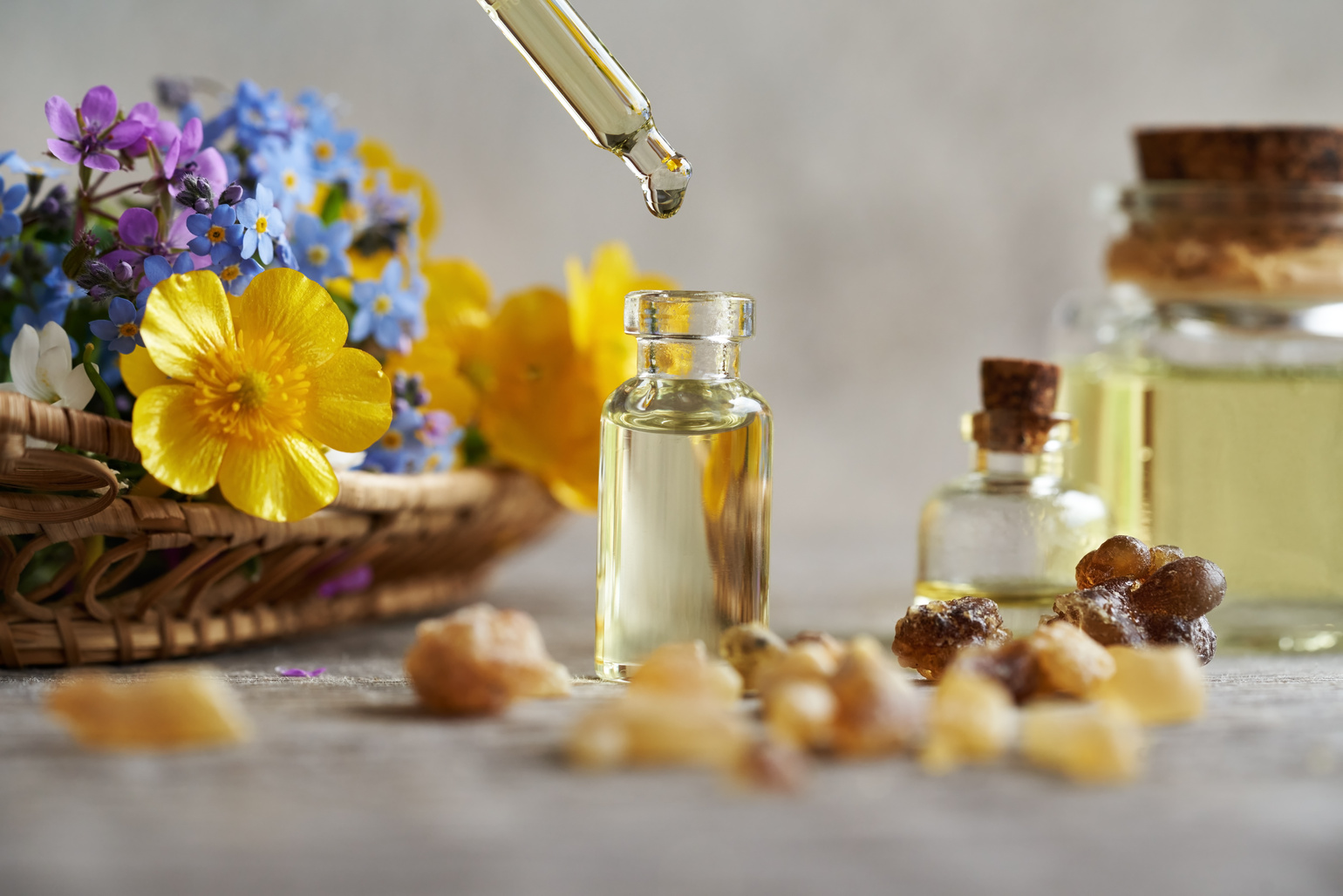 Dropping essential oil into a bottle, with frankincense and colorful flowers